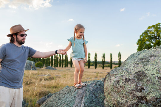 Dad helping daughter climb lichen covered boulders in soft sunset light