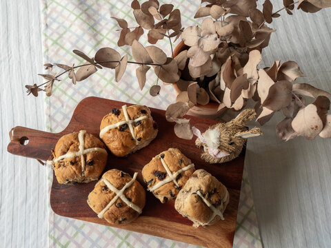 Hot cross buns on wooden serving tray with dried eucalyptus and rabbit decoration on table top