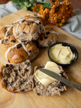 Hot cross buns on cutting board with butter and knife and orange flowers in background