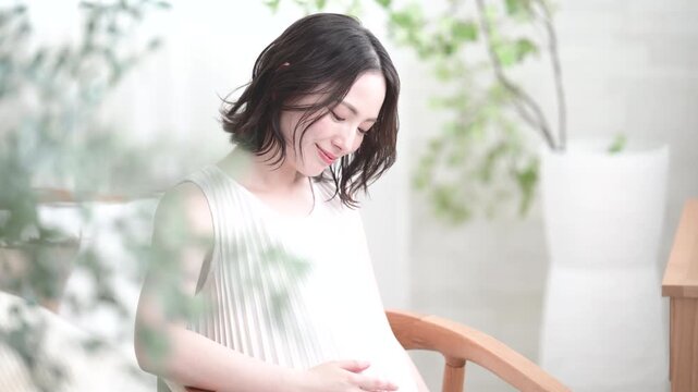 [スローモーション]笑顔でお腹に手を添える日本人女性の妊婦さん、マタニティライフスタイルイメージの笑顔で座る動画