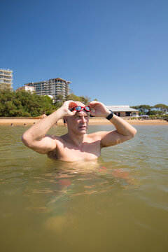 Male open water swimmer wearing goggle standing in water near the shore