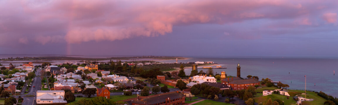 Aerial view of a rainbow in a dramatic coloured sky over historic buildings in a coastal town