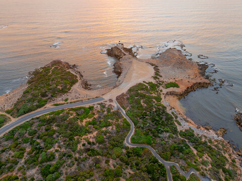 Aerial view of a road and walking tracks around a rugged coastline at dusk