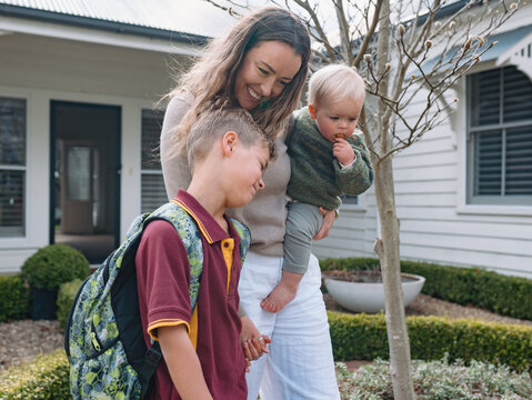 Aussie mum walking with young son while carrying her toddler on her hip to do school drop-off