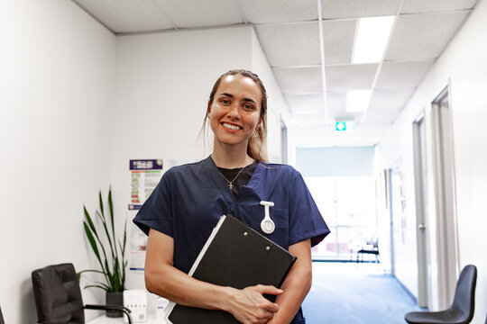 Healthcare professional with clipboard smiling in clinic hallway