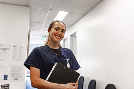 Aboriginal nurse in navy scrubs holding clipboard in hospital hallway