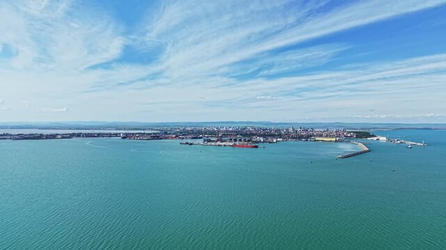 Aerial island skyline over turquoise ocean, cirrus clouds sweeping across clear blue sky, calm water with subtle reflections, small boats near harbor
