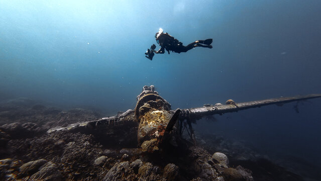 Scuba diver hovers above the coral-encrusted engine and wing of a sunken WWII Japanese plane