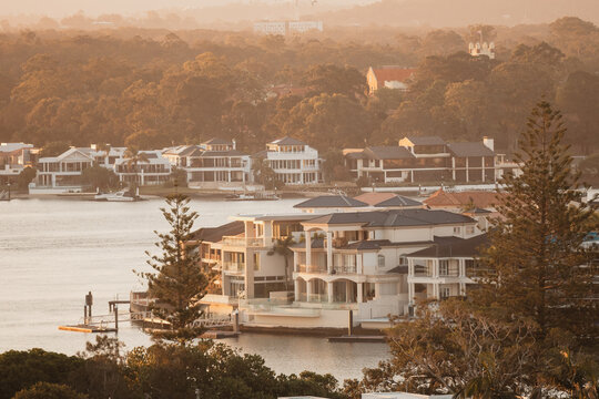 Luxury waterfront mansions line a serene river at golden hour