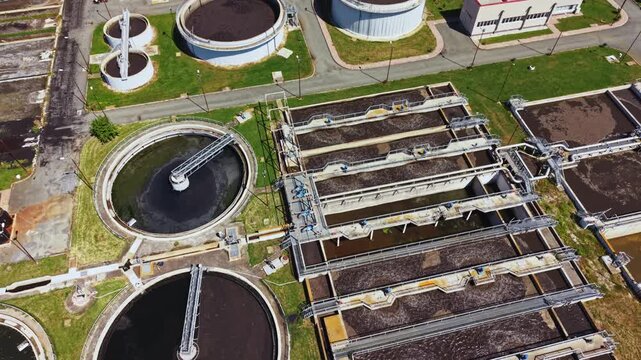 Aerial view sewage treatment plant showing circular clarifiers and aeration basins with rotating mixers, rectangular settling beds, green buffer zones, access