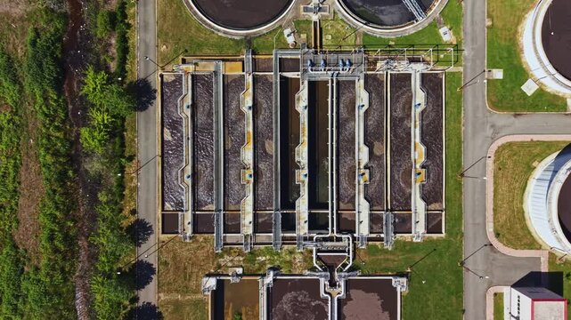 Top down view sewage treatment complex with circular digesters and aeration basins, methane tanks and processing ponds, grassy service corridors, monitoring