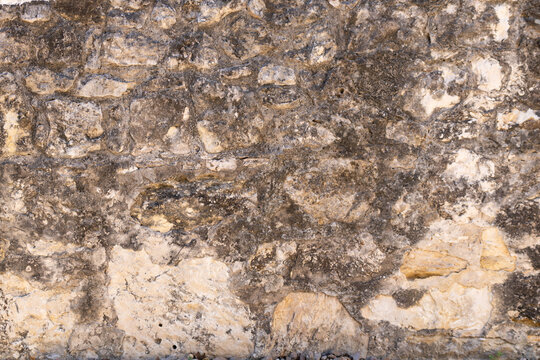 Rugged weathered rubble stone wall with mottled grey and tan masonry texture