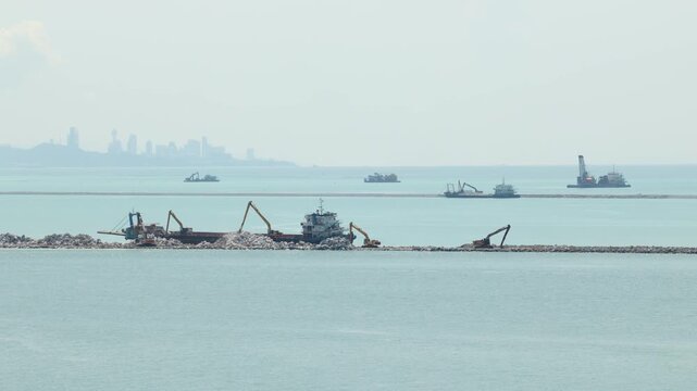 Industrial Dredging Ships Working On A Coastal Breakwater Construction Project Near A City Skyline