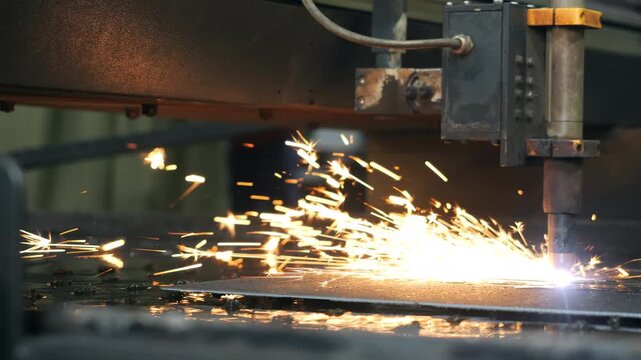 Industrial CNC plasma cutting machine cutting metal sheet with bright sparks during automated metal fabrication in factory.