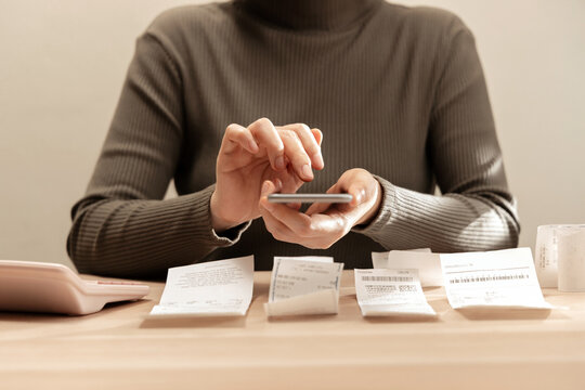 Women using smartphone calculate paper receipts on table. Calculating bills, expense tracking, personal finance