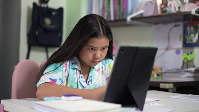 asian child student studdy online by tablet or teenager has acne writing on book or young kid girl learn from home with computer by video call and write or people homeschool studying to back to school