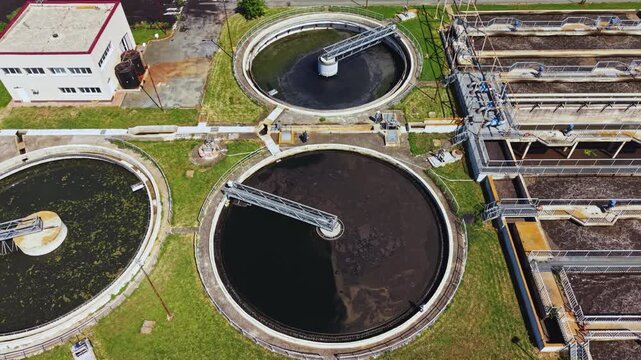 Aerial sewage treatment plant circular clarifiers with rotating arms, dark sludge in basins, aeration structures, concrete channels and piping, drone