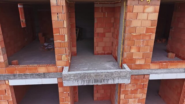 Unfinished brick apartment construction site showing exposed rooms, concrete slabs, stacked bricks, scattered debris, empty doorways contractor inspection vibe,