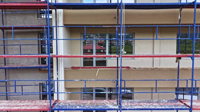 Scaffolding wrapped commercial facade during retrofit, blue metal frames and glass panels visible, crew harnesses and hoist equipment in use, cladding removal