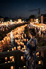 Obraz premium 夏祭りの小川のほとりを歩く浴衣姿の日本人女性 | Japanese women in yukata walking along the banks of a stream during a summer festival Generative AI