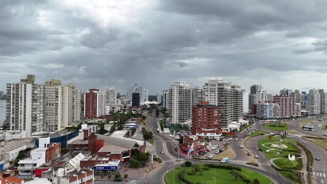 PUNTA DEL ESTE, URUGUAY: High-angle drone view of the urban skyline featuring Torre El Torreon, luxury high-rise apartments, green roundabouts, and the ocean horizon under a cloudy sky.