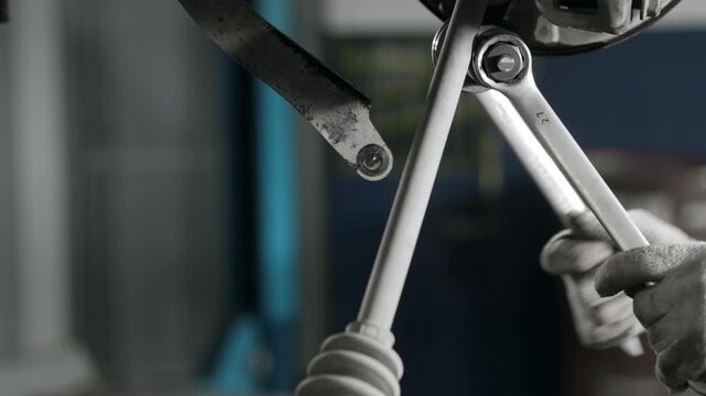 Detailed close up of mechanic hands repairing vehicle suspension system with wrenches in auto service workshop.