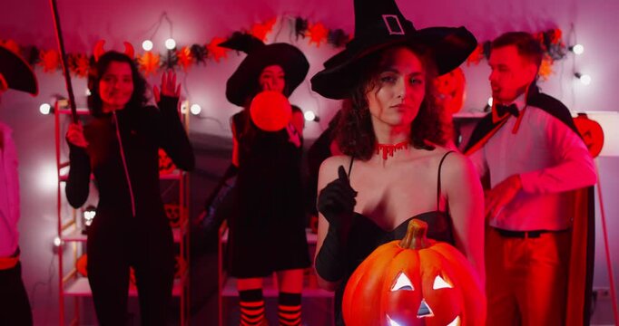 Portrait of a happy woman in a witch costume holding a pumpkin at a halloween dance party at home.Festive Atmosphere, celebrating in a fun and cheerful setting filled with excitement and holiday.