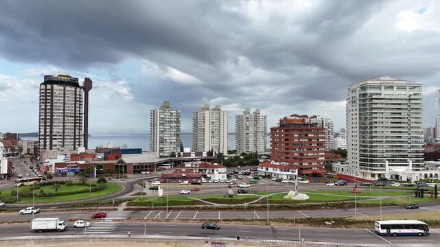 PUNTA DEL ESTE, URUGUAY: High-angle drone view of the urban skyline featuring Torre El Torreon, luxury high-rise apartments, green roundabouts, and the ocean horizon under a cloudy sky.