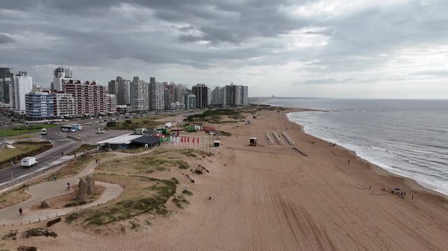PUNTA DEL ESTE, URUGUAY: Aerial drone view of Playa Brava beach featuring the famous Fingers Sculpture on the sand, with Atlantic ocean waves and beachfront luxury high-rise buildings.