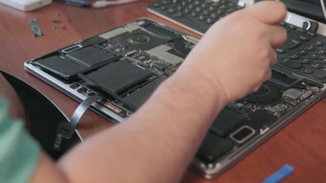 Hands of a technician dismantling a lithium-ion laptop battery using a special tool in a service center