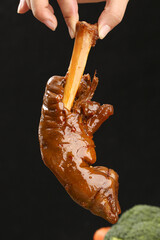 Fototapeta premium Hand Holding Marinated Lamb Meat Cooked in Rich Brown Sauce on Black Background