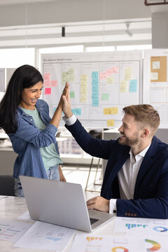 Two laughing workmates giving high five in office, express recognition and satisfaction teamwork and cooperation, celebrate success in business and career. Interpersonal synergy between team members