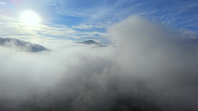 A breathtaking aerial drone perspective soaring over a dense, expansive sea of low-hanging morning clouds, with majestic mountain peaks breaking through the mist under a clear, bright sunrise sky. Thi