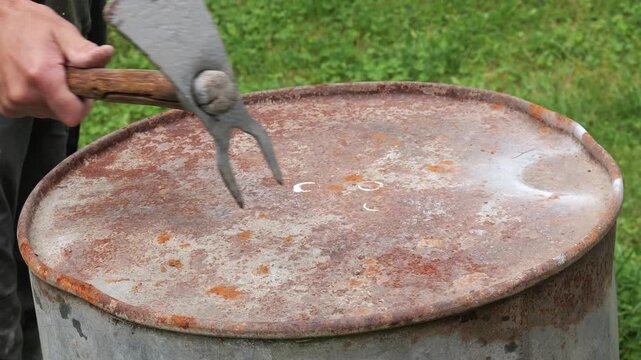 Farmer piercing rusty metal drum lid with grub hoe tool