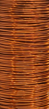 Detailed macro view of tightly coiled copper wire with a shiny reddish‑orange metallic surface. The parallel layers create a striking linear pattern, highlighting copper&rsquo;s reflective texture.