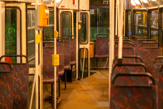 Interior view of an empty vintage tram showing rows of passenger seats with patterned blue and red upholstery, metal handrails, yellow ticket validators, and warm overhead lighting.