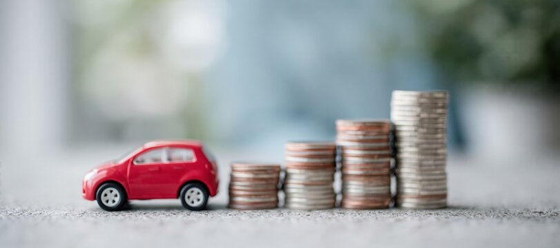 Red toy car beside increasing stacks of coins symbolizing car loan interest or savings