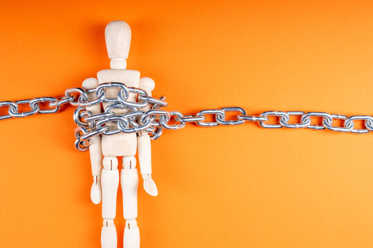 Chained wooden figure on orange backdrop, oppression and loss of autonomy symbolism