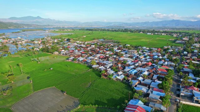 Aerial drone footage of Bolo village area and main road, a vast salt pond field valley nearby the sea, in Sumbawa, Indonesia, and green rice fields aside, mountains behind with Bima city bay