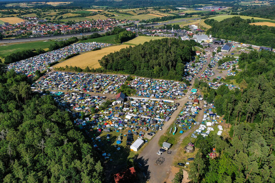 Geiselwind, Germany - 21 June 2025: Aerial view of Eventzentrum Strohofer Geiselwind musichall with a crowded campsite, lush green forests, and rolling hills under a clear sky.
