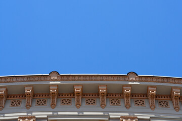 Low angle view of a decorative architectural roof cornice with stone ornaments and brackets on a historic building under a clear blue sky. © nahhan