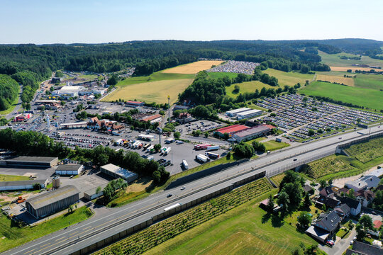 Geiselwind, Germany - 21 June 2025: Aerial view of Eventzentrum Strohofer Geiselwind musichall with extensive parking lots and the highway surrounded by green fields and forests.