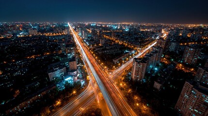 Fototapeta premium Aerial view of a busy city highway interchange at night with glowing light trails from traffic, illuminating the urban landscape.