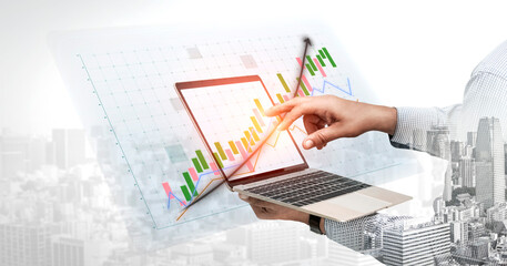 Obraz premium A hand interacts with a laptop displaying a vibrant data chart overlay, symbolizing the fusion of technology and finance in a busy urban setting. Impute
