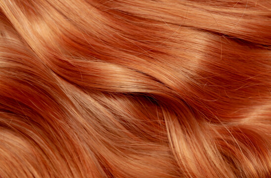 Red hair close-up as a background. Women's long orange hair. Beautifully styled wavy shiny curls. Hair coloring bright shades. Hairdressing procedures, extension.