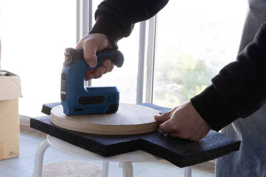 Electric tacker fixing black covering material onto a wooden surface near a window