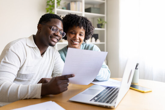 Happy couple reading documents and working on laptop at home