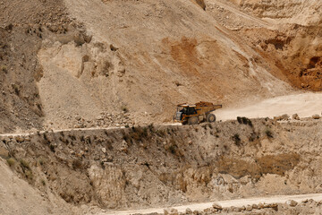 Heavy mining dump truck transporting excavated material along haul road inside active limestone quarry. Industrial mining operation with terraced excavation walls and earthmoving activity. © Ekaterina