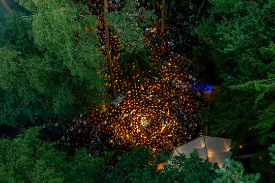 Herzogenaurach, Germany - 27 July 2025: Aerial view of the Open Beatz Festival with a large crowd gathered among tall trees in a forest illuminated by warm lights.