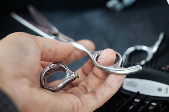 Close-up of a barber's hand holding professional silver hair cutting scissors.